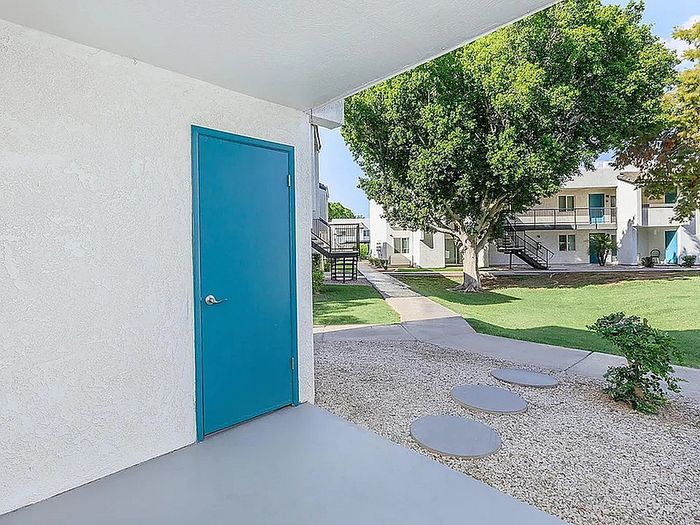 Charming apartment entryway with vibrant blue door, lush green lawns, and modern outdoor pathways, perfect for a serene living experience.