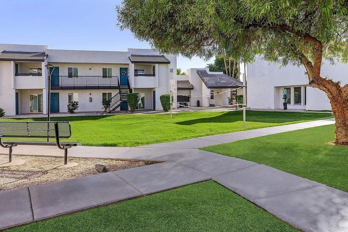 Charming apartment complex with modern architecture and lush green surroundings, featuring a spacious courtyard and inviting outdoor seating.