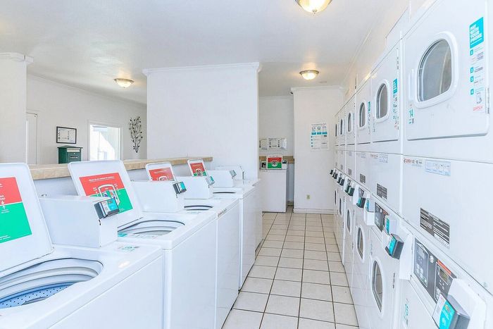 Spacious and well-lit laundry room with modern washing machines and dryers in a clean, tile-floored environment.