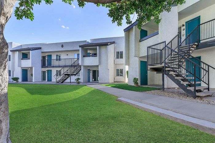 Modern apartment complex with lush green lawns, featuring sleek staircases and a crisp white exterior.