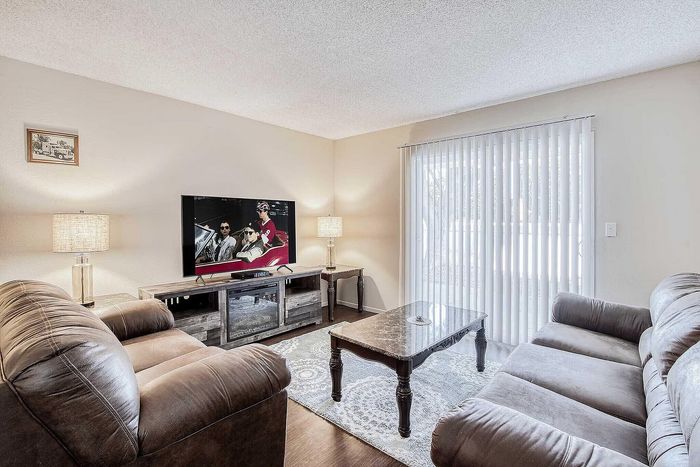 Inviting living room with cozy brown sofas, sleek TV setup, elegant lamps, and large windows offering natural light.