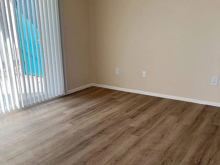 Bright and airy room with elegant wood flooring and large vertical blinds leading to a patio.