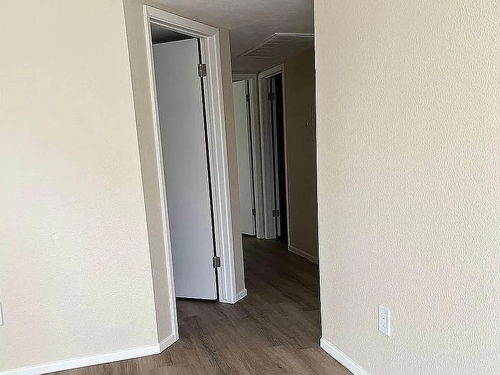 Inviting apartment hallway with sleek wooden flooring and neutral walls, leading to multiple rooms for versatile living.