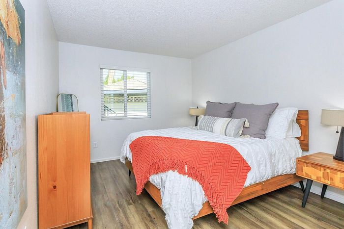 Bright and cozy bedroom featuring modern wood furniture, vibrant artwork, and a comfortable bed with plush pillows and a colorful throw.