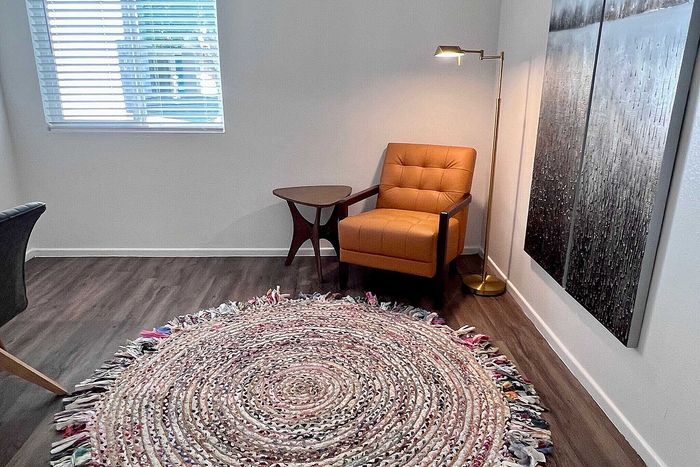 Cozy living space featuring a stylish orange armchair, unique round woven rug, elegant floor lamp, and modern artwork.