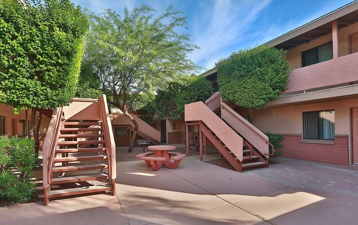 Charming apartment courtyard featuring lush greenery, twin staircases, and a cozy picnic area.