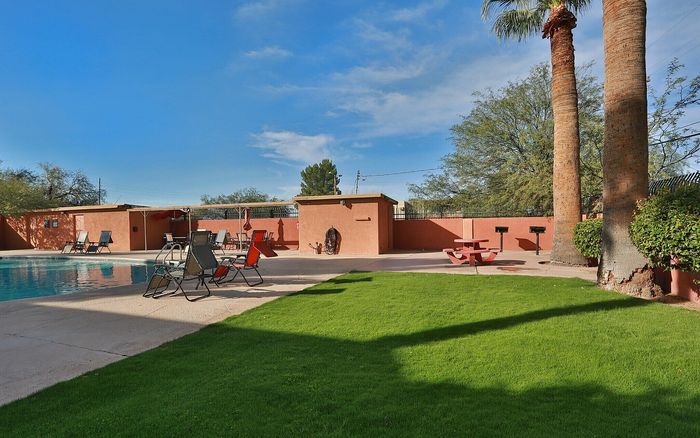 Inviting poolside oasis with comfortable lounge chairs, lush green lawn, and shaded picnic area under clear blue skies.