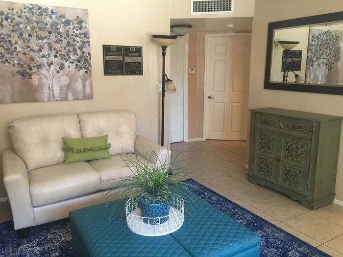 Cozy living room with elegant decor; features a cream sofa, green pillows, vibrant artwork, and a chic patterned cabinet.