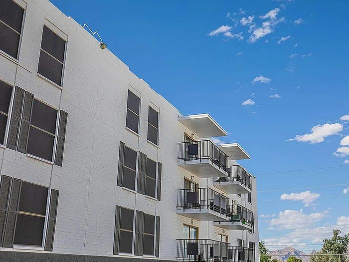 Charming white brick apartment building with spacious balconies under a bright blue sky, offering scenic views and modern urban living.