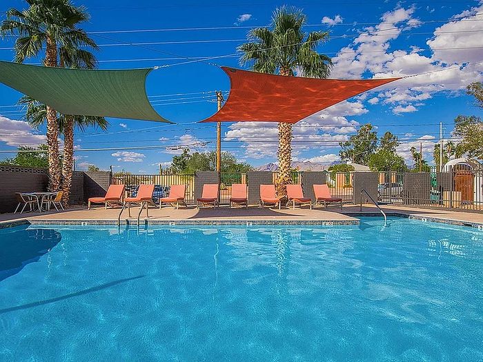 Inviting outdoor swimming pool with vibrant sun loungers and shaded areas, perfect for relaxation under clear blue skies.