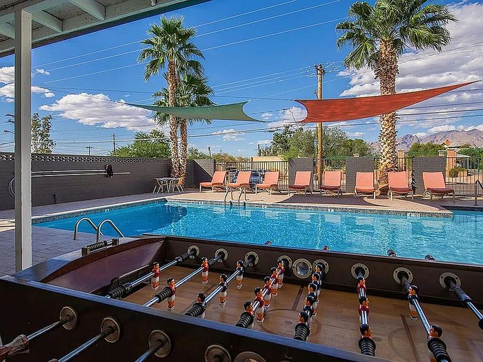 Luxurious poolside oasis with foosball table, stylish sun loungers, and vivid shade sails under a bright blue sky.