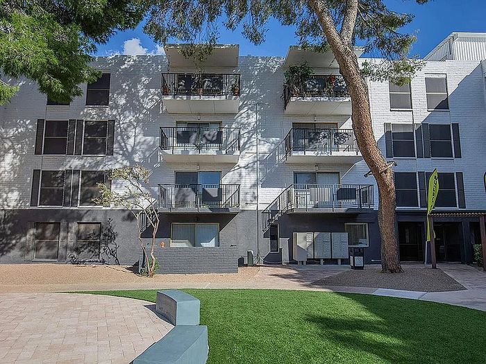 Modern apartment building with charming balconies, lush green landscaping, and sunny courtyard view.