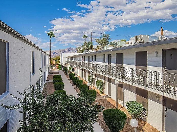 Charming apartment complex with a mountain view, featuring manicured hedges, palm trees, and a sunlit walkway.