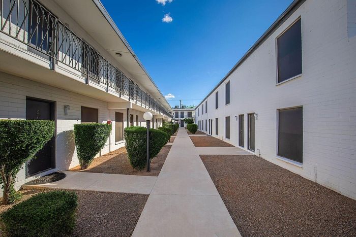 Charming apartment complex with modern architectural design, featuring well-manicured hedges and expansive walkways under a bright blue sky.