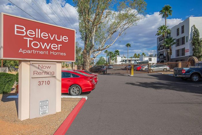Inviting Bellevue Tower Apartment Homes entrance with vibrant signage and ample parking under a sunny sky, now renting.