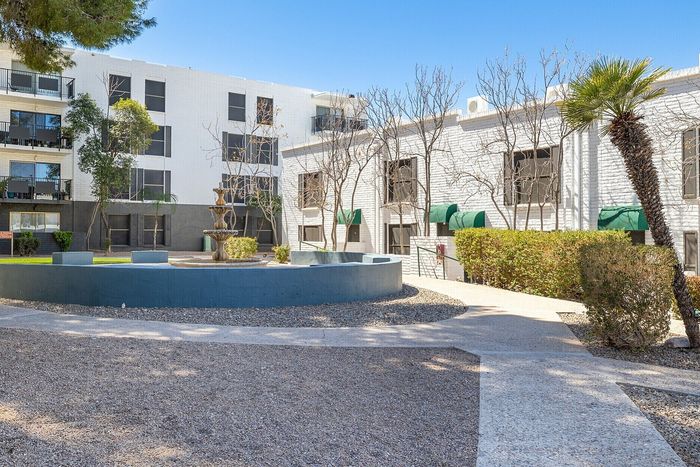 Inviting apartment complex exterior featuring a charming courtyard with a fountain, lush greenery, and modern architecture under a clear blue sky.