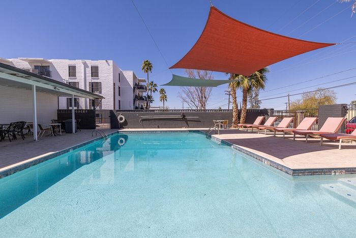 Luxurious apartment complex with a pristine outdoor pool, stylish sun loungers, and shaded sitting areas, perfect for relaxation under clear blue skies.