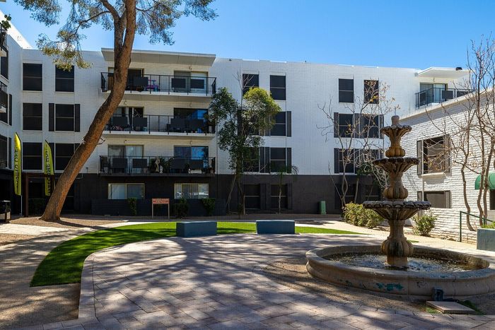 Beautiful apartment courtyard with a vibrant green lawn, elegant water fountain, and modern white brick architecture under a clear blue sky.