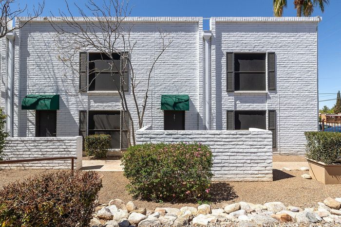 Charming white brick apartment building with lush green landscaping and inviting curb appeal.