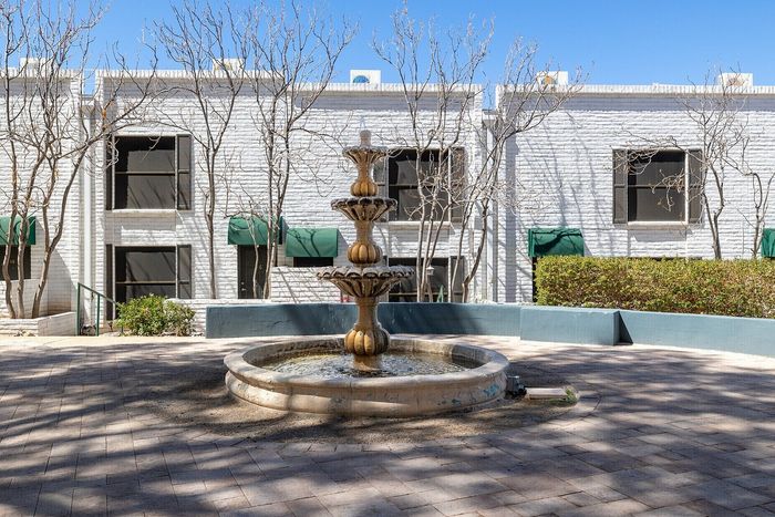 Charming outdoor courtyard with a classic multi-tiered fountain, surrounded by lush greenery and stylish white brick buildings.