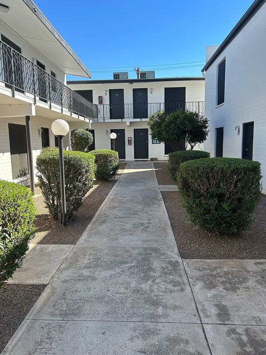 Charming apartment complex with modern architecture, featuring a clean walkway and lush shrubs under a bright blue sky.