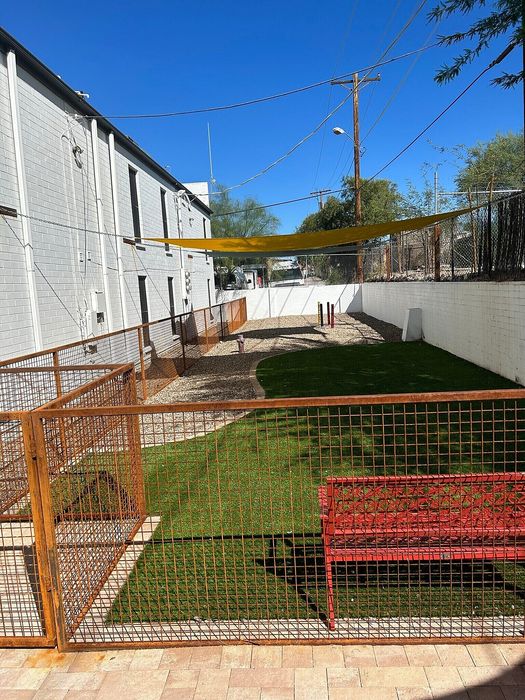 Inviting outdoor space featuring green artificial turf, a vibrant red bench, and rustic metal fencing under a clear blue sky.