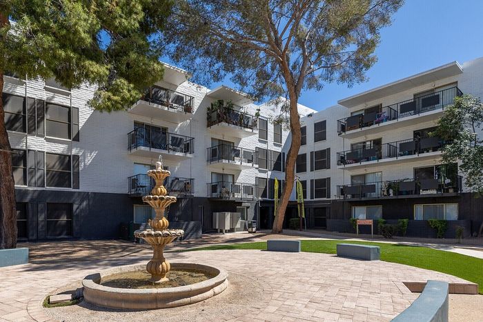Charming apartment complex with modern white facade, private balconies, and a classic stone fountain in the sunny courtyard.
