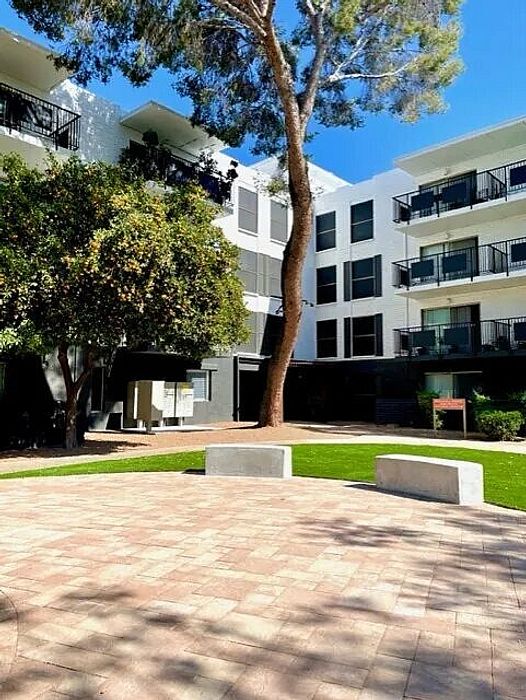 Charming apartment complex with modern balconies, lush greenery, and serene courtyard setting under a bright blue sky.
