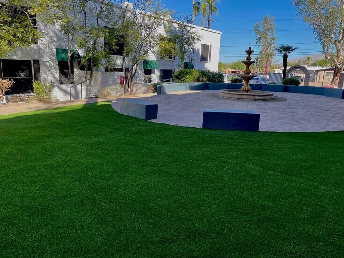 Charming courtyard view featuring a circular fountain, lush green lawn, and elegant building facade with trees and palm background.