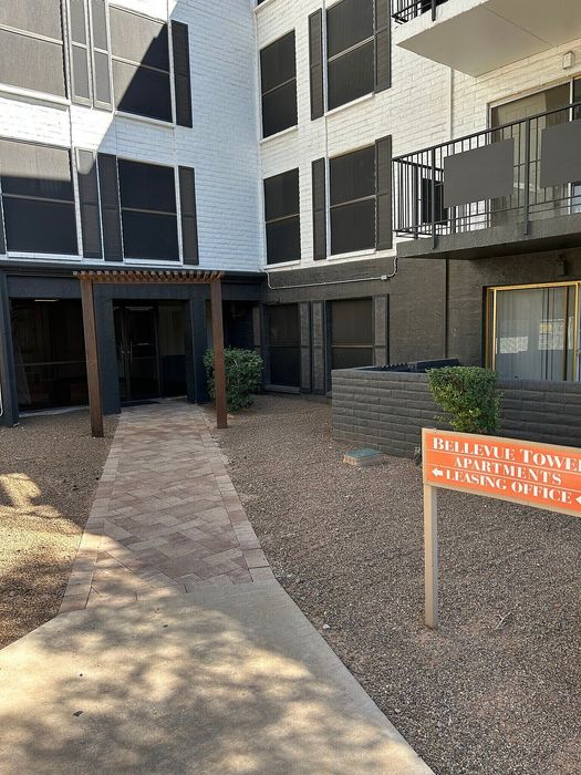 Inviting brick pathway leading to the modern entrance of Bellevue Tower Apartments, surrounded by elegant architecture and lush greenery.