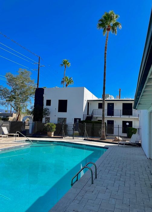 Inviting apartment complex with a sparkling blue swimming pool, palm trees, and modern architecture under a clear blue sky.