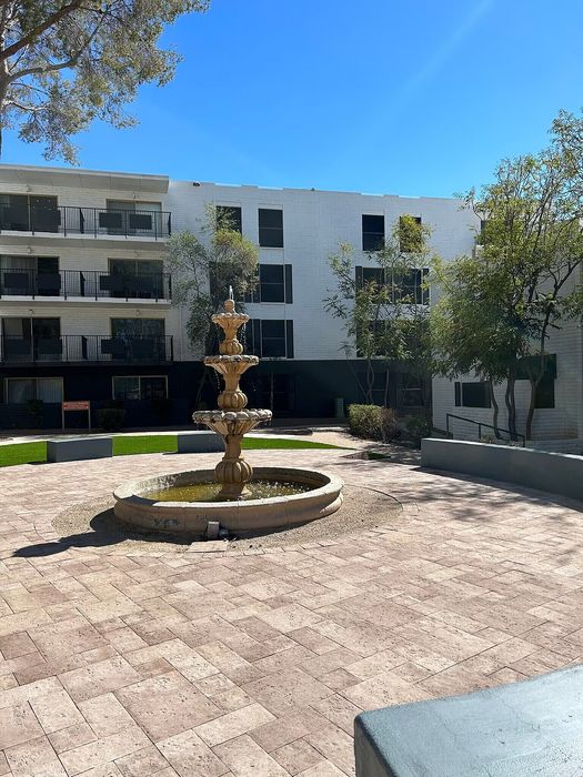 Charming courtyard with elegant tiered fountain surrounded by lush greenery and modern apartment balconies under a clear blue sky.