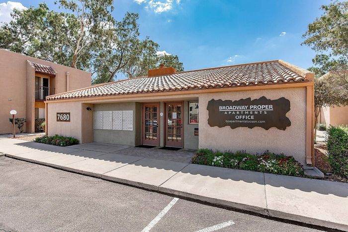 Charming apartment office with a welcoming facade, lush landscaping, and ample mailbox storage, nestled under a clear blue sky.