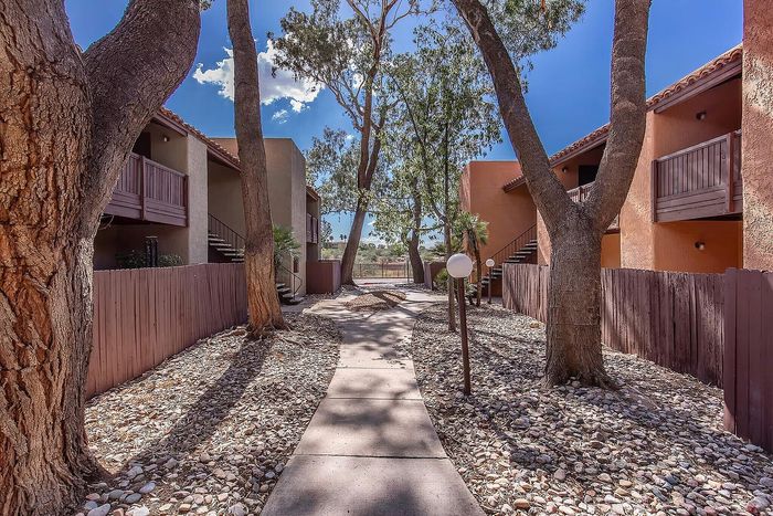 Charming apartment complex with rustic wooden balconies, surrounded by tall trees and a well-maintained pathway.