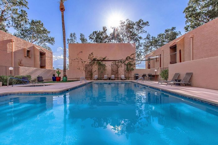 Inviting swimming pool with lounge chairs, surrounded by lush greenery and modern architecture under a clear blue sky.