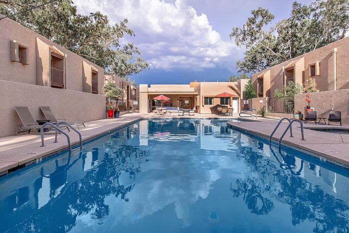 Inviting apartment complex with a sparkling outdoor pool, sun loungers, and vibrant umbrellas, surrounded by lush greenery and modern architecture.