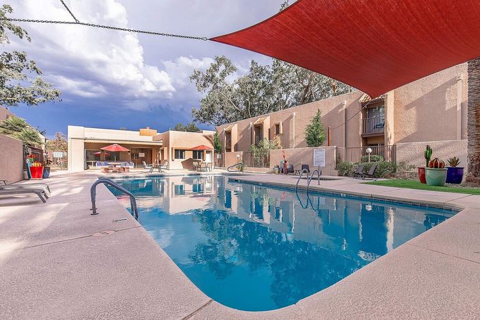 Inviting outdoor pool area with modern lounge chairs, shaded canopy, and vibrant landscaping in a serene apartment community.