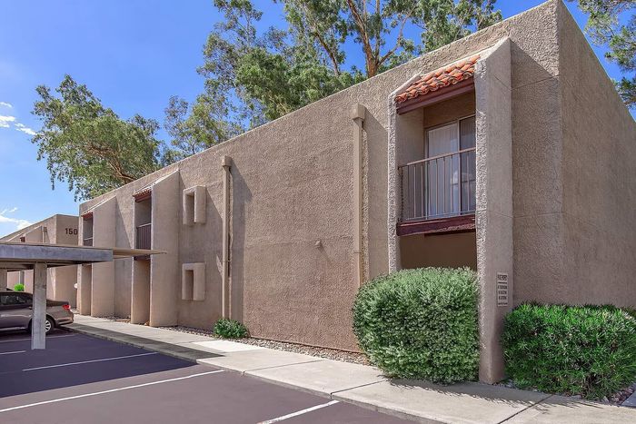 Charming apartment exterior with unique stucco design, shaded balconies, and lush greenery in a serene parking area.