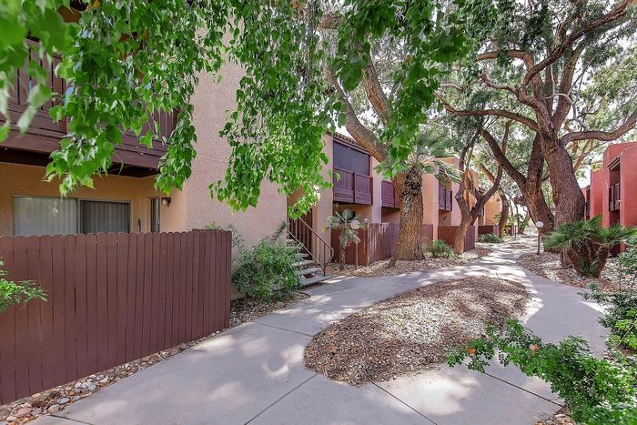 Charming apartment complex walkway surrounded by lush greenery and mature trees, offering serene outdoor spaces.