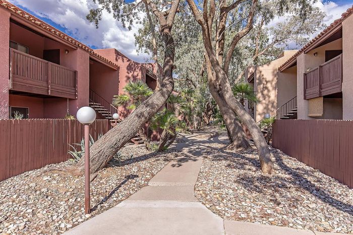Charming apartment complex with rustic wooden balconies, nestled amidst lush landscaping and winding walkways under a clear blue sky.