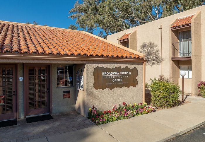 Charming entrance of Broadway Proper Apartments office with warm terracotta roof and vibrant floral landscaping.