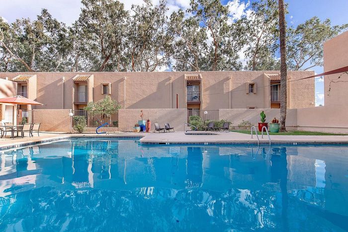Inviting apartment complex showcasing a sparkling blue swimming pool, modern lounge chairs, and lush greenery against a backdrop of sunlit architecture.