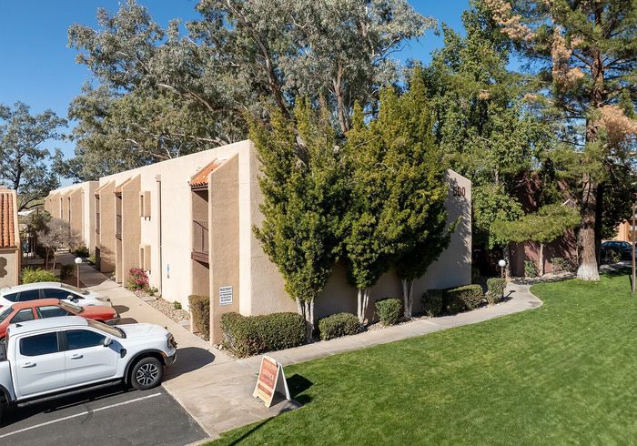 Charming apartment complex with lush greenery, spacious parking, and modern architecture under a clear blue sky.