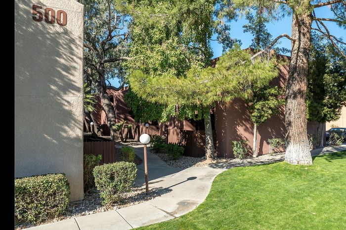 Charming apartment entrance surrounded by lush greenery and a welcoming pathway, nestled in a tranquil neighborhood setting.