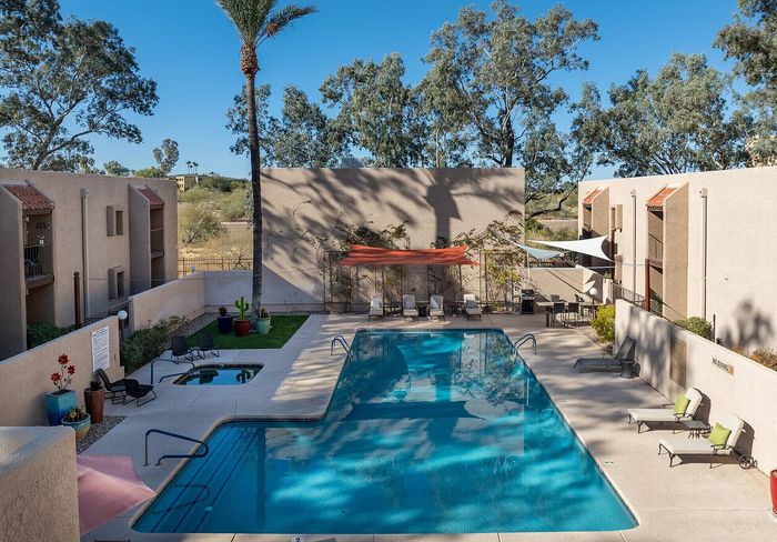 Elegant apartment complex with a stunning outdoor pool, surrounded by lush greenery and stylish lounge areas.