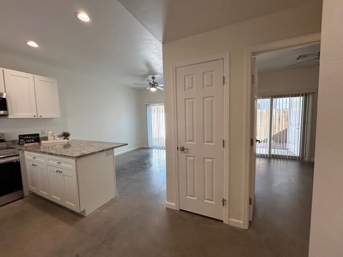 Contemporary apartment interior showcasing a sleek kitchen with granite countertops, spacious living area with ceiling fan, and bright rooms with sliding glass doors.