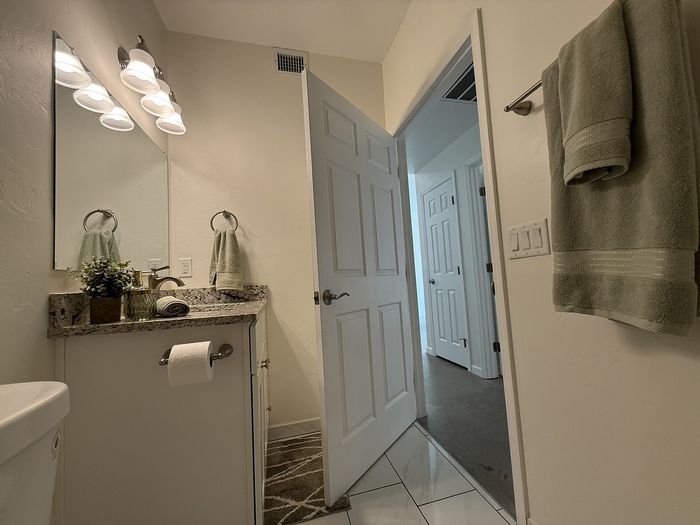 Elegant bathroom with a granite countertop, stylish lighting, and plush towels, leading into a bright hallway.