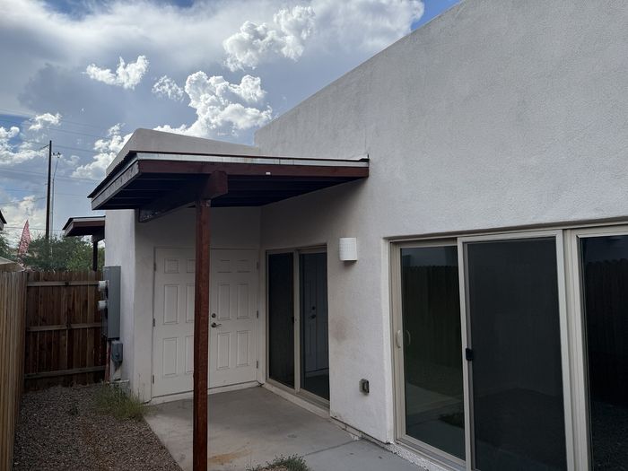 Modern exterior of apartment with sleek white walls, covered entryway, and large sliding glass doors, set against a stunning sky backdrop.
