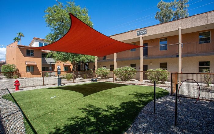 Charming apartment exterior with a vibrant shade canopy, lush green dog park, and attractive landscaping, perfect for pet lovers.