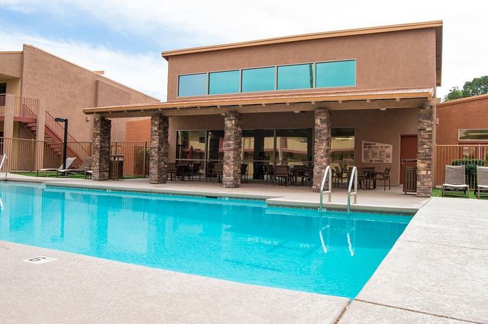 Luxurious apartment complex featuring a sparkling outdoor swimming pool and stylish covered patio area with cozy seating.